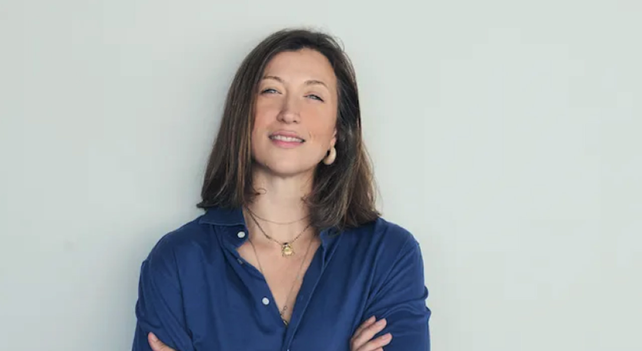 Portrait de la philosophe Marie Robert, souriante, chemise bleue, sur fond clair